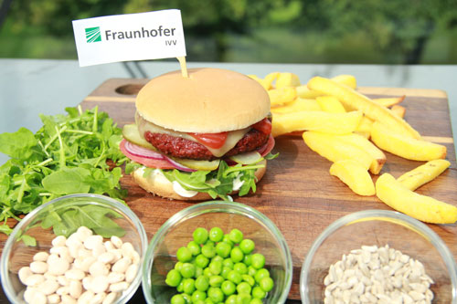 Ein veganer Burger mit Fraunhofer IVV-Papierfähnchen, Pommes, davor drei Glasschälchen mit den verwendeten veganen Zutaten