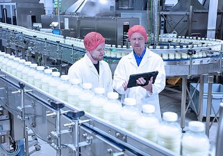 Zwei Forscher in weißen Kitteln und mit roter Haube betrachten in einem Technikum mit Plastikflaschen befüllt mit Milch die datenbasierte Maschinenanalyse für effiziente und nachhaltige Produktion