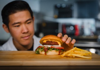 Ernährung der Zukunft-veganen Fleischalternativen Ein Burger mit veganem Patty sowie Pommes auf Schneidebrett