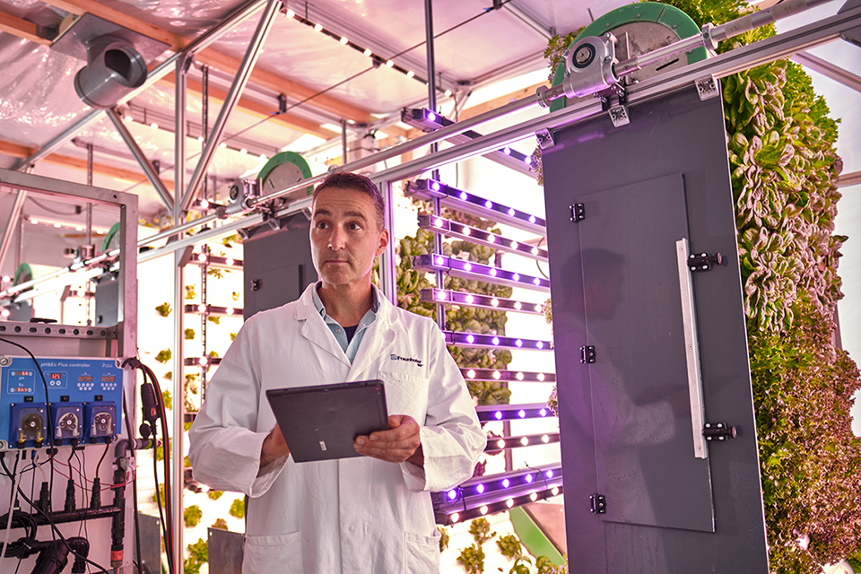 Mann mit Tablet vor Vertical-Farming-Anlage