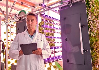 Mann mit Tablet vor Vertical-Farming-Anlage