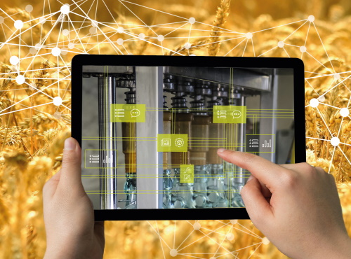Zwei Hände halten ein Tablett, über den digital Flaschenbfüllmaschinen gesteuert werden können, im Hintergrund ist ein Weizenfeld.