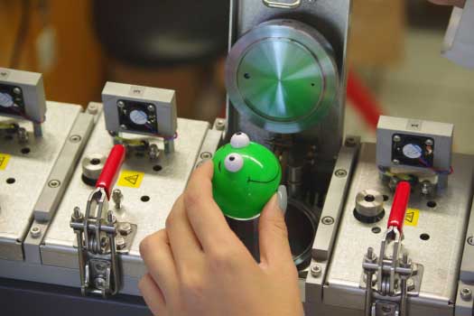 Eine Hand gibt ein grünes rundes Plastikspielzeug in eine Mikrokammer zur Analyse