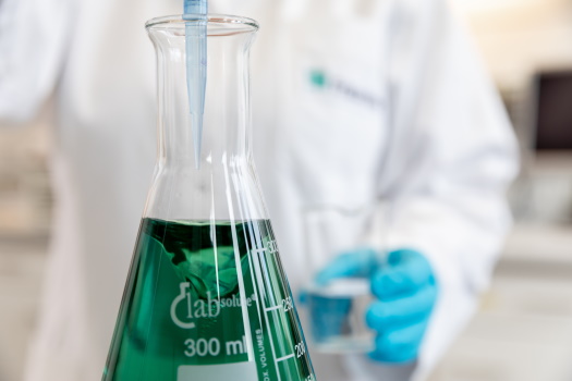 Extraktion von Pflanzenstoffen für biobasierte Schmierstoffe Erlenmeyerkolben, gefüllt mit grüner Flüssigkeit, welche von Mitarbeiter hinzugefügt wird
