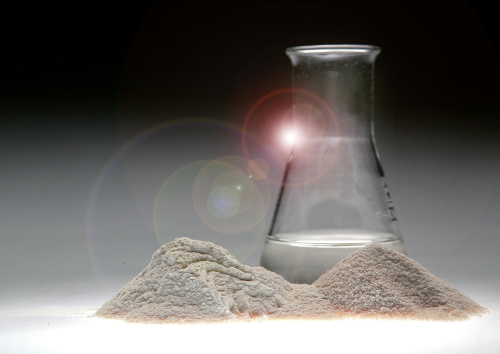 Two piles of baobab powder in front of a conical flask containing liquid