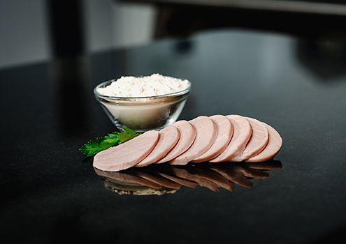 Sausage slices without nitrite, with a small bowl of plant extracts in the background