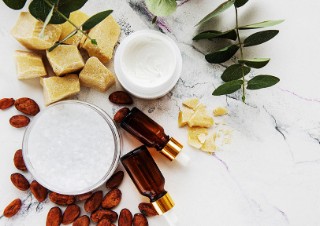 Cream jars, small brown vials and cocoa butter and cocoa beans lie on natural stone