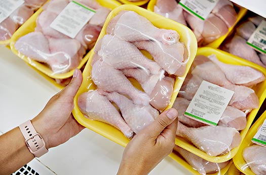 Two hands hold chicken thighs packed in PLA trays with shrink film