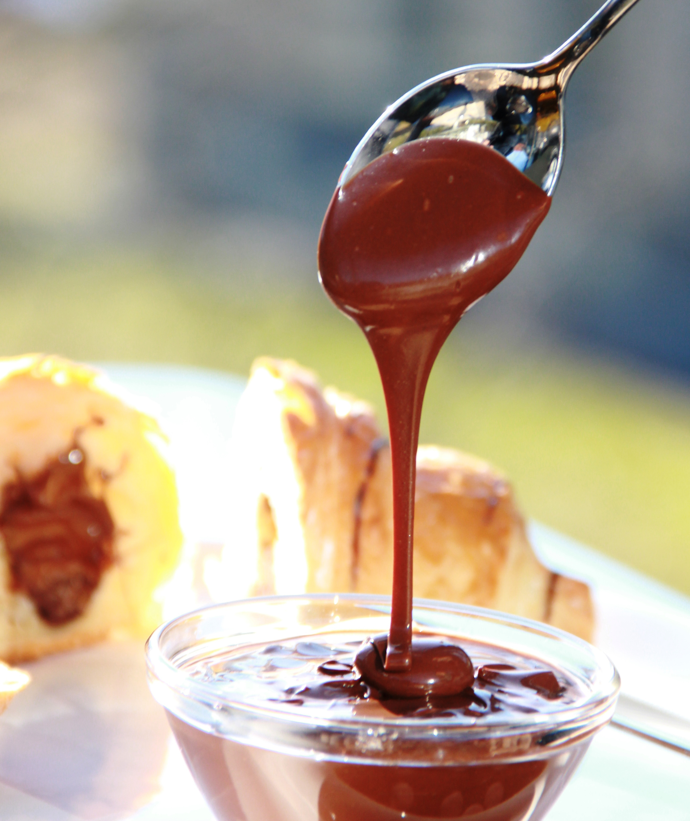 Nut nougat cream flows from a spoon into a small glass bowl.