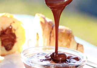 Nut nougat cream flows from a spoon into a small glass bowl.