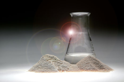 Erlenmeyer flask with cloudy liquid, in front of it differently coarsely ground beige powder 